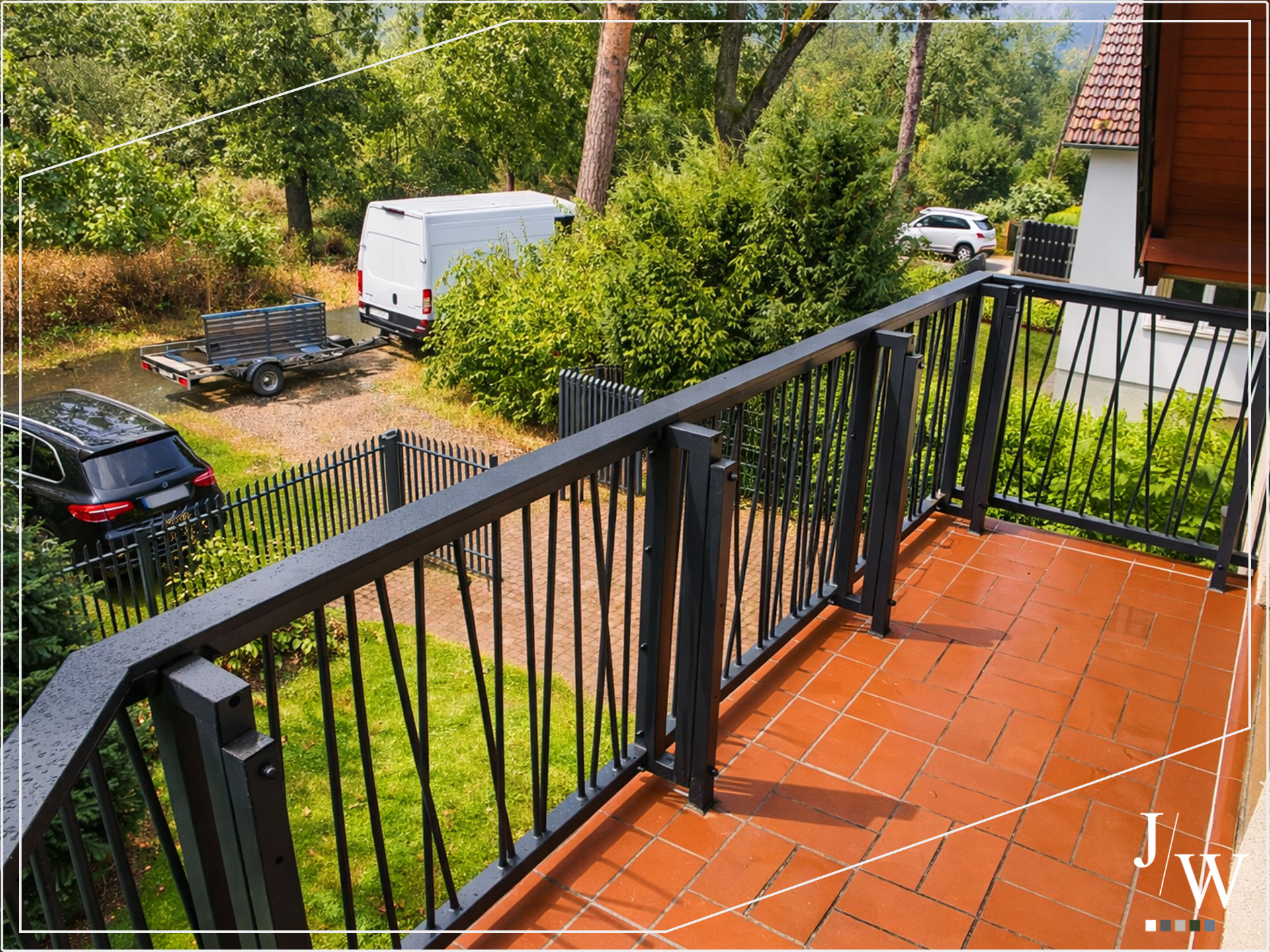 Balkongelaender aus Stahl in Anthrazit auf einem gefliesten Balkon, modernes Design mit vertikalen Dekorelementen und Blick in den Gartenbereich und Einfahrt