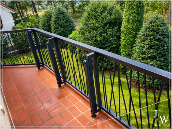 Balkongeländer in Anthrazit auf einem gefliesten Balkon, modernes Design mit vertikalen Dekorelementen und Blick in den Gartenbereich.
